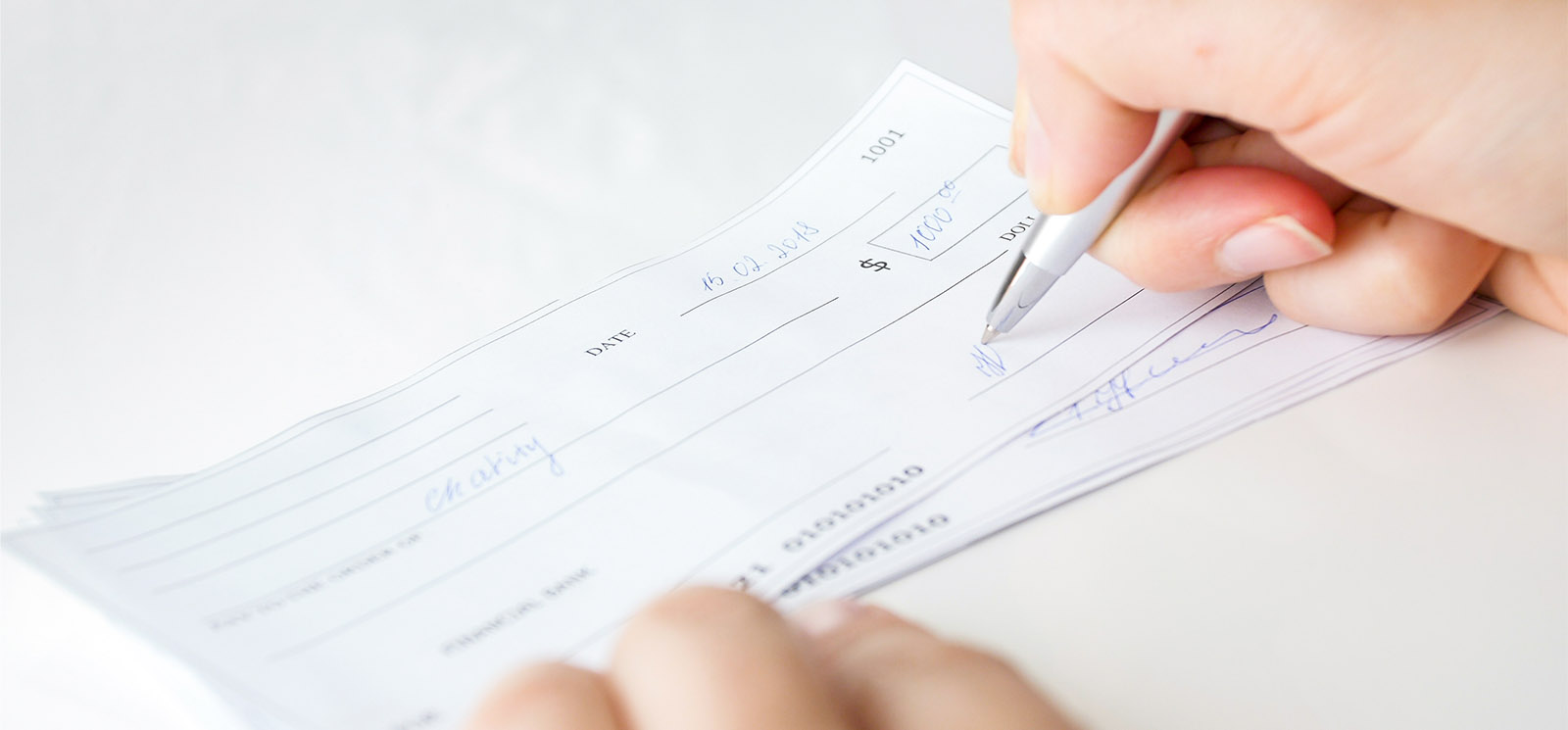 Closeup image of businesswoman putting her signature on personal bank cheque with pen