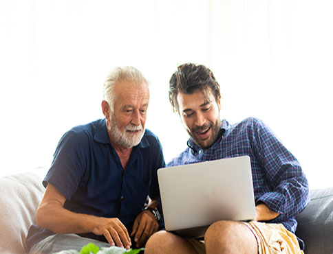 Father and son sitting on a couch looking at a laptop computer together.